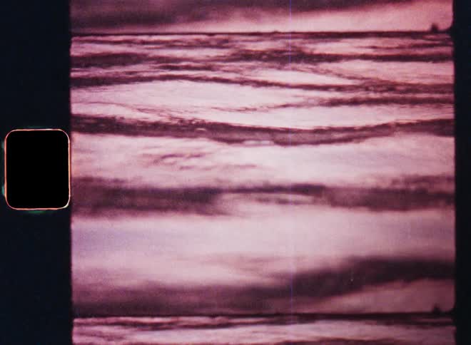 In the serene twilight a body of water reflects the fiery hues of the red sky while the rippling surface of the lake river sea or ocean moves due to waves rolling into the shore