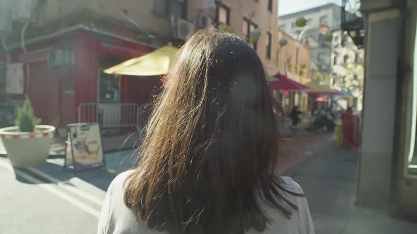 A woman with dark wavy hair and wearing a white shirt walks down the street in the downtown area of the city