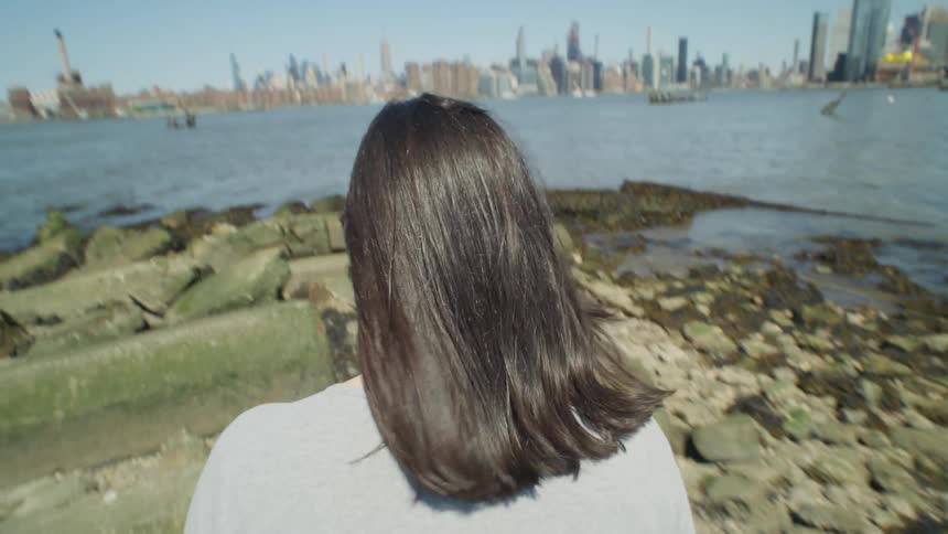 A woman navigates the rocky shoreline near NYC skyline