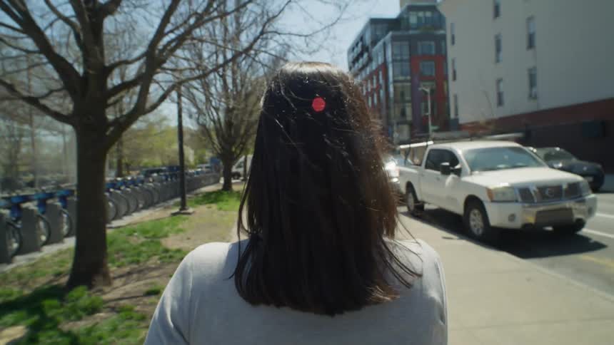 A woman walks down an urban city street next to a park