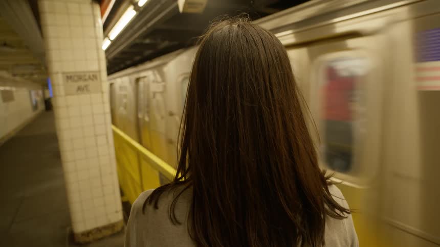 Perspective of a blackhaired woman seen from behind at a station with a train arriving