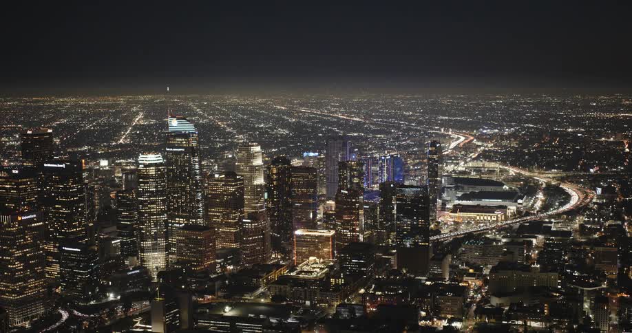 A sweeping aerial panorama shows the downtown Los Angeles skyline, the 110 Freeway, the Los Angeles Convention Center, and Crypto.com Arena