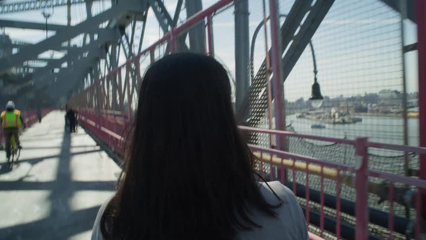 A woman viewing the city skyline ahead as she walks across the Williamsburg Bridge in New York City
