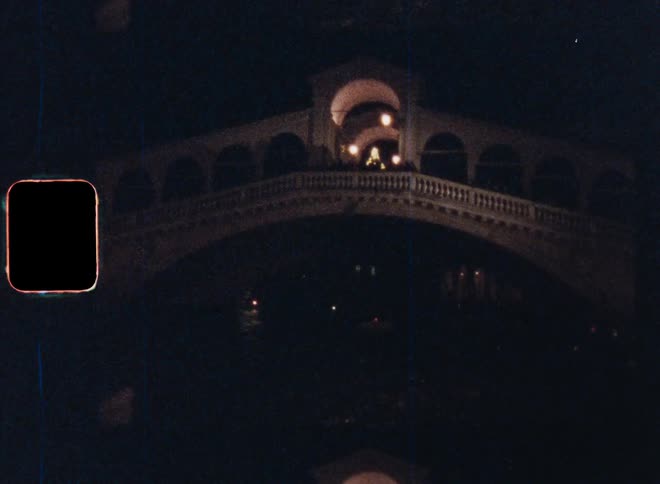 Driving on a ferry or boat on the water under the Rialto bridge a famous landmark in Venice that is illuminated with golden lights at night on Super 8 film