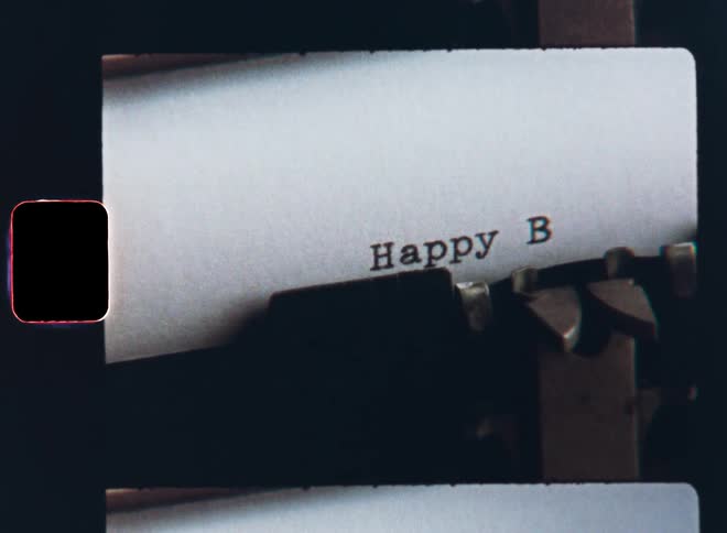 Old Super-8 film footage of a retro typewriter typing the expression or words Happy Birthday on a sheet of paper for a card or letter expressing empathy and wishing a happy anniversary to the birthday child