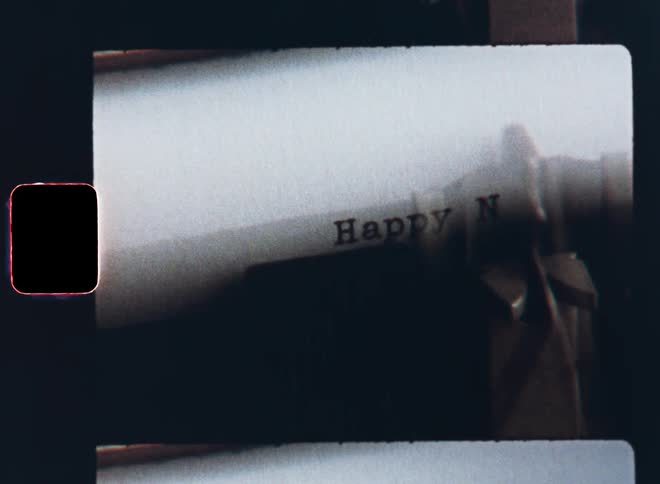 Old super 8mm film footage close-up of the mechanical writing parts of an analogue typewriter typing the words Happy New Year on a white sheet of paper as part of a celebration letter or while manifesting good resolutions