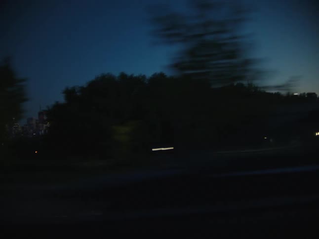 Moving view on a road or dusk with silhouette of trees and vehicles