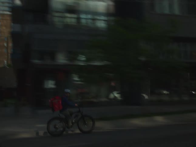 Delivery man riding a bicycle on the street of a metropolis with buildings around