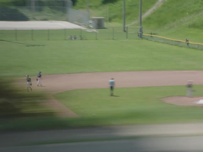 A baseball game in progress on a green field with players seen from a moving vehicle
