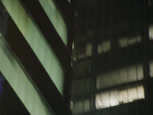A vehicle speeds through the downtown area of the city passing illuminated skyscrapers at night