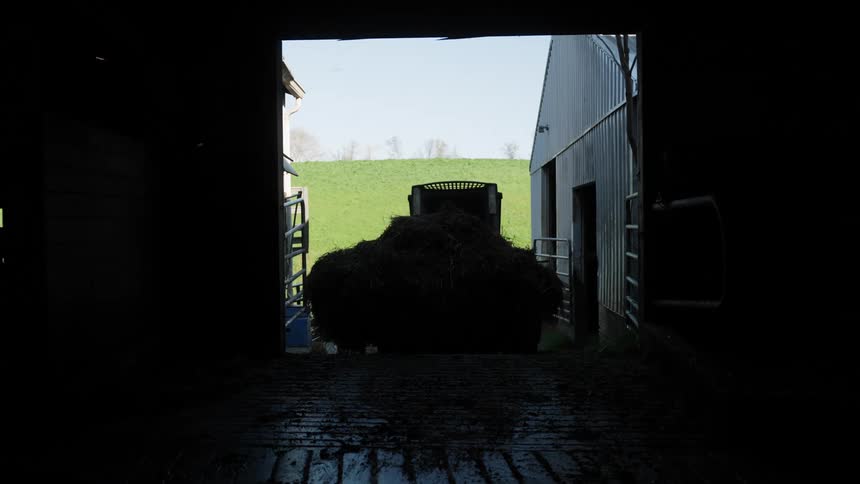Man driving a small tractor carrying dry straw into a shed