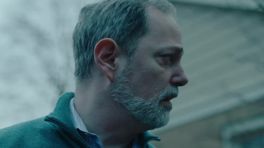 A sad person in a jacket is standing outdoors at dusk