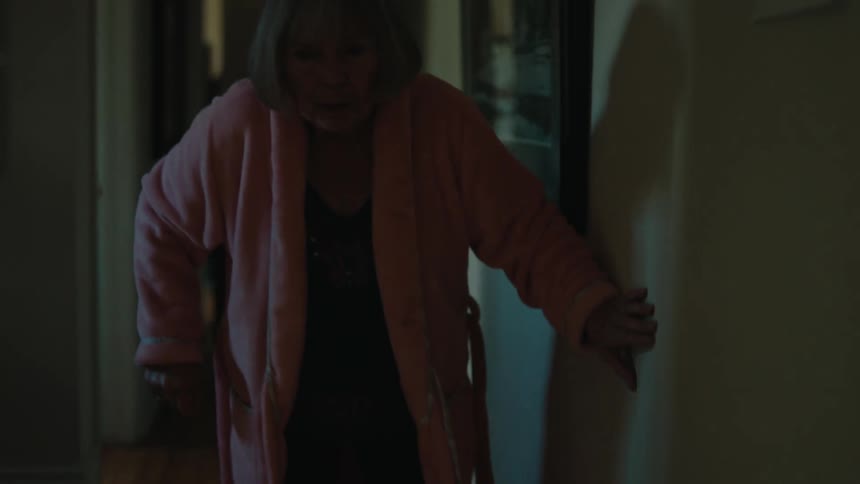 An elderly woman holds the wall as she walks down the hallway