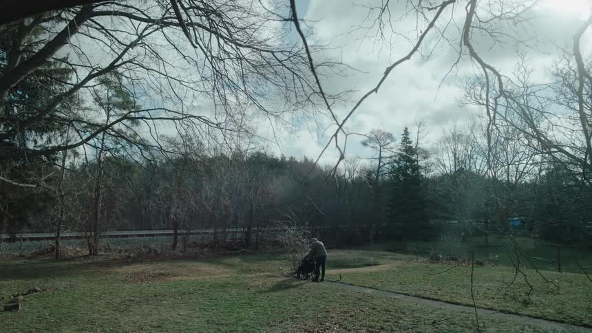 A man rolls a person in a wheelchair across a backyard