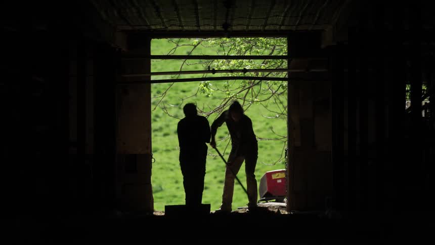 Two men sweep out the barn