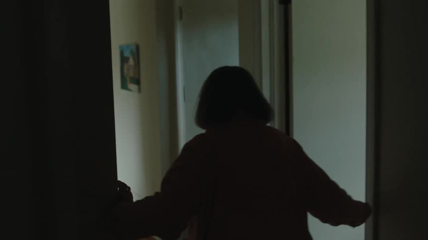 A woman is turned away wearing a pink coat and walking down a hallway
