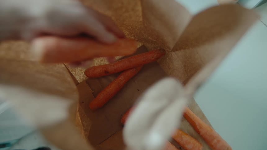 Womans hand sticking carrots inside a cardboard bag