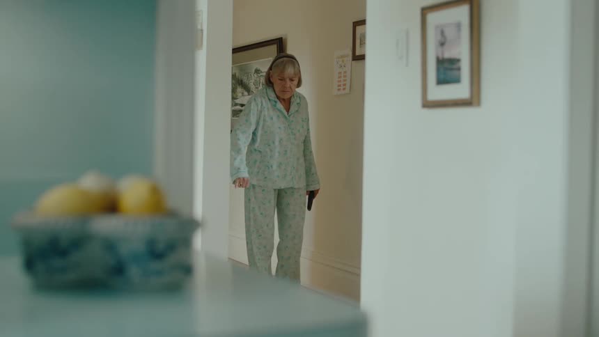 A woman wearing pajamas walks down her hallway
