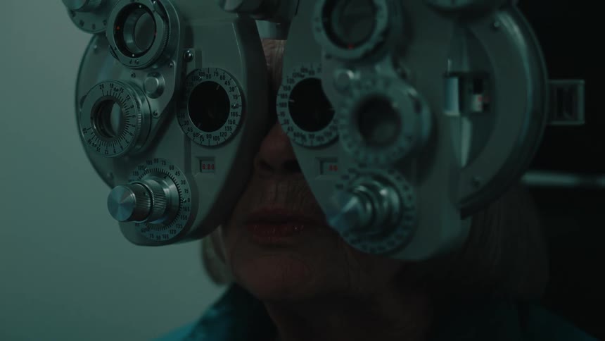 A person is undergoing an eye examination with a phoropter in a dimly lit room