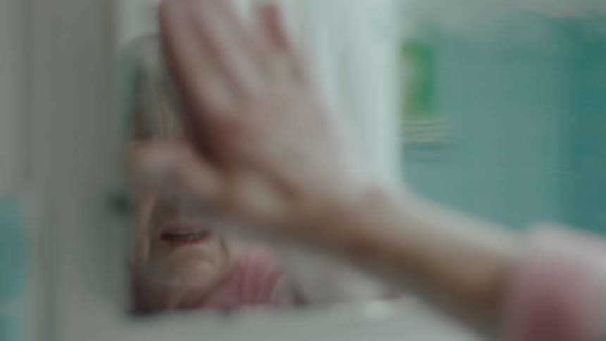 An elderly woman cleans a bathroom mirror with her hand