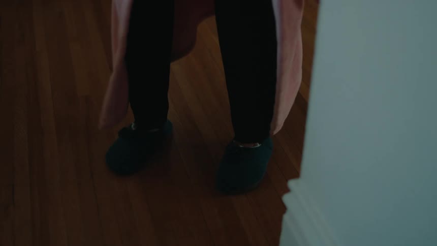Legs of an elderly woman in slippers walking slowly down the hallway of the house