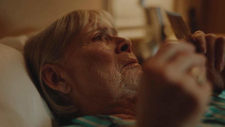 Elderly woman lying in bed frowns while looking at photograph then puts it on the side table