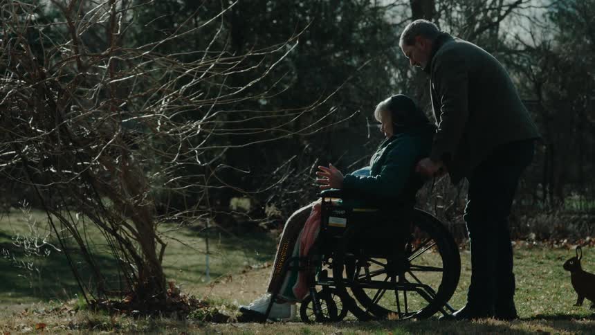 A man pushes a woman in a wheelchair from the home