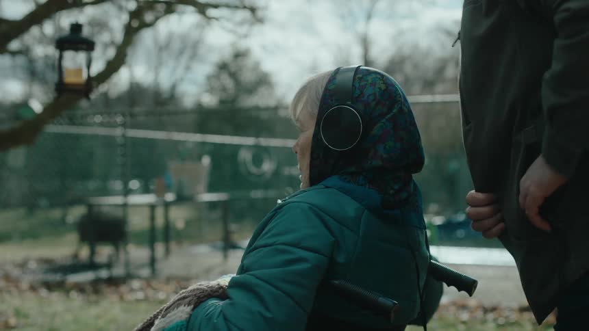 Man putting headphones on a lady who is sitting in a wheelchair in a park