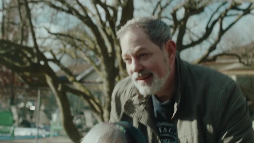 A man pushing a wheelchair with an elderly woman in a neighborhood