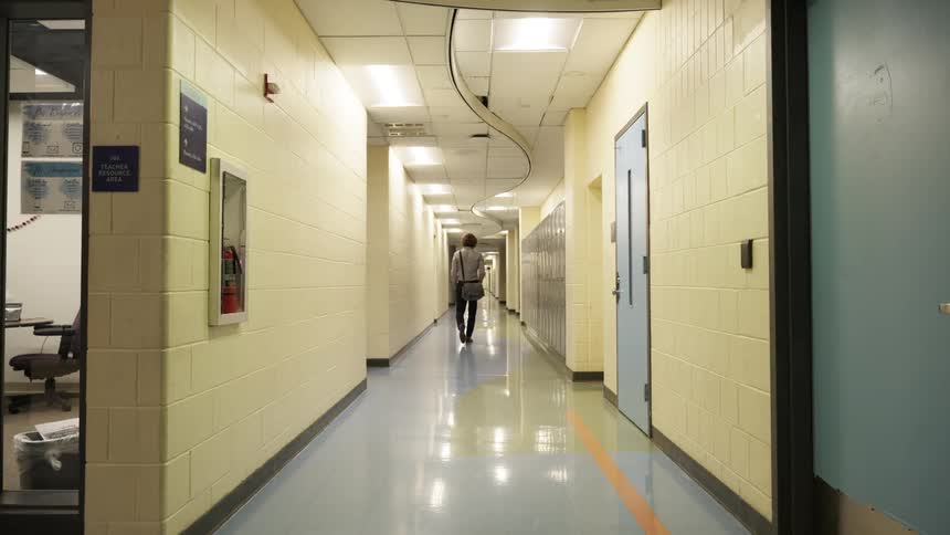 A male teacher walks down an empty school hallway