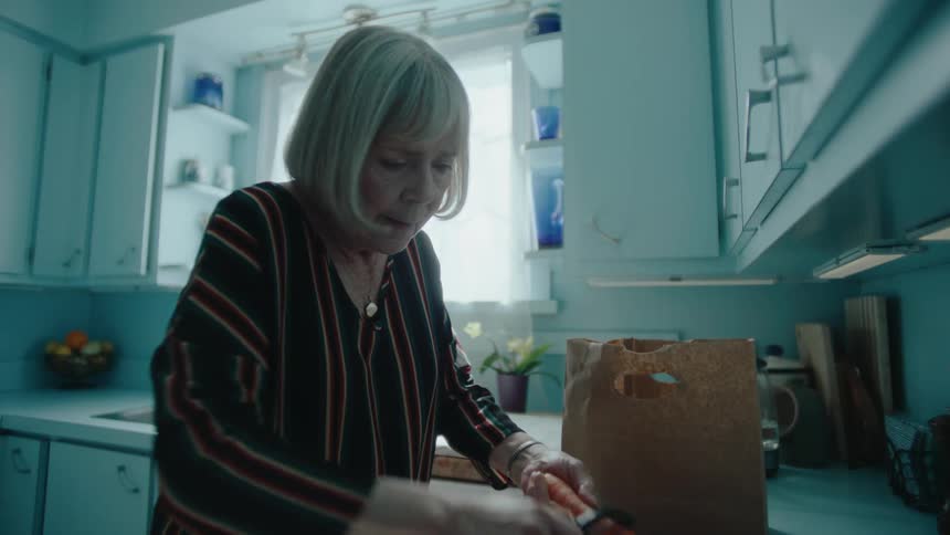 An elderly lady peels and tastes a fresh carrot in the kitchen at home