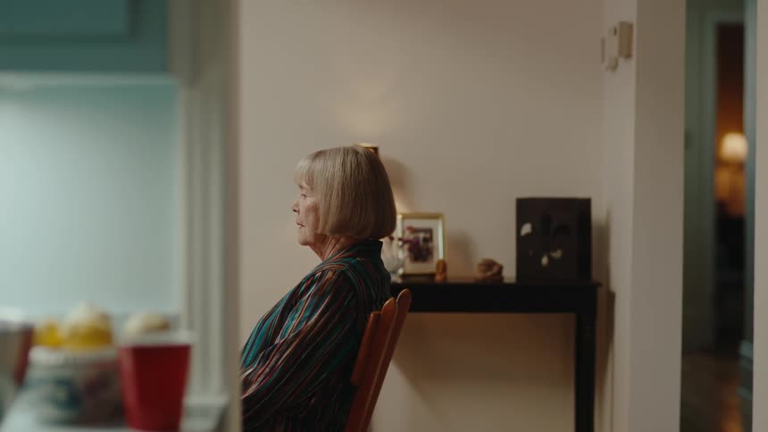 Elderly woman sitting in home sighs after looking over her shoulder