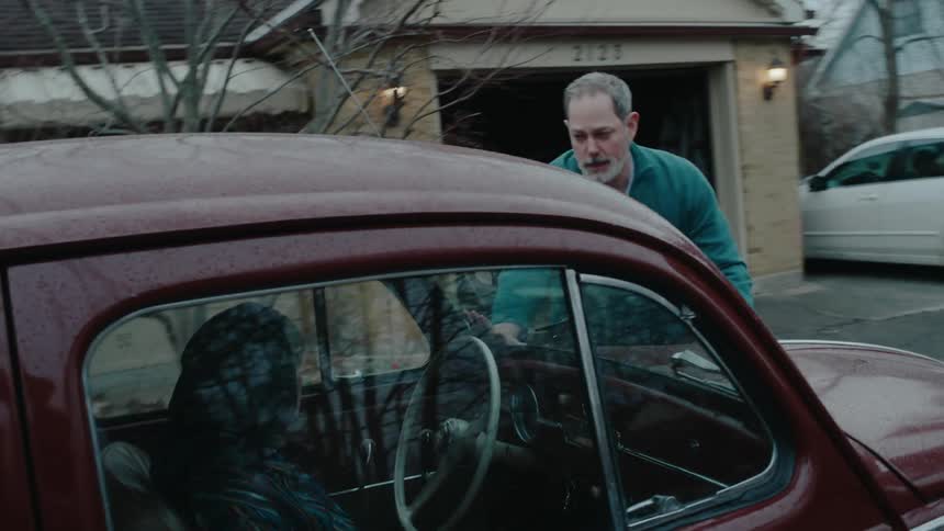 Man leaving the garage running towards a woman who is inside a stopped car