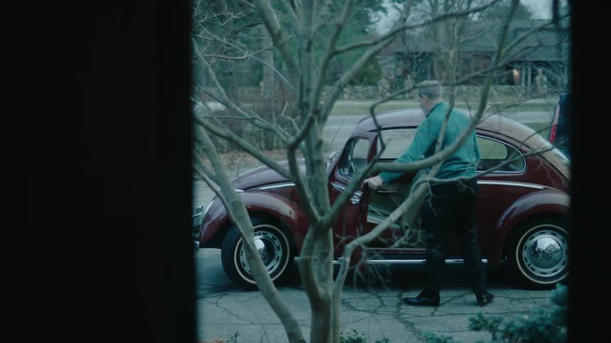 View from the window of a man getting into a beetle parked on the edge of a house