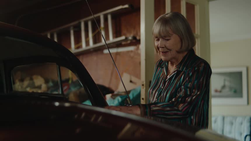Elderly woman enters a garage to admire a parked car