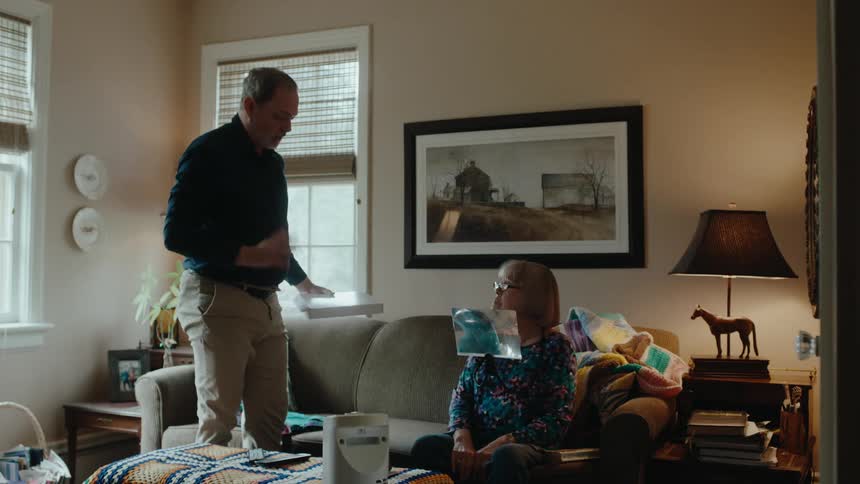 Man arguing with an elderly woman who is sitting on the sofa using a metal support on her body that she then removes