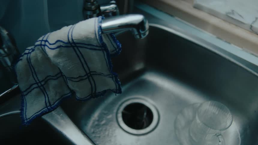 A stainless steel kitchen sink with a leaky faucet and a dishcloth hanging from it