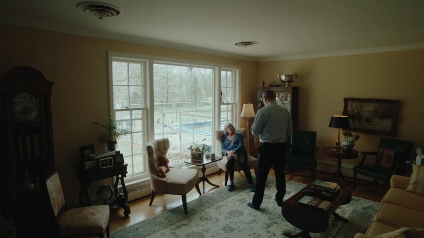 Elderly man sitting in an armchair in the living room and a man coming in taking a support for the blind