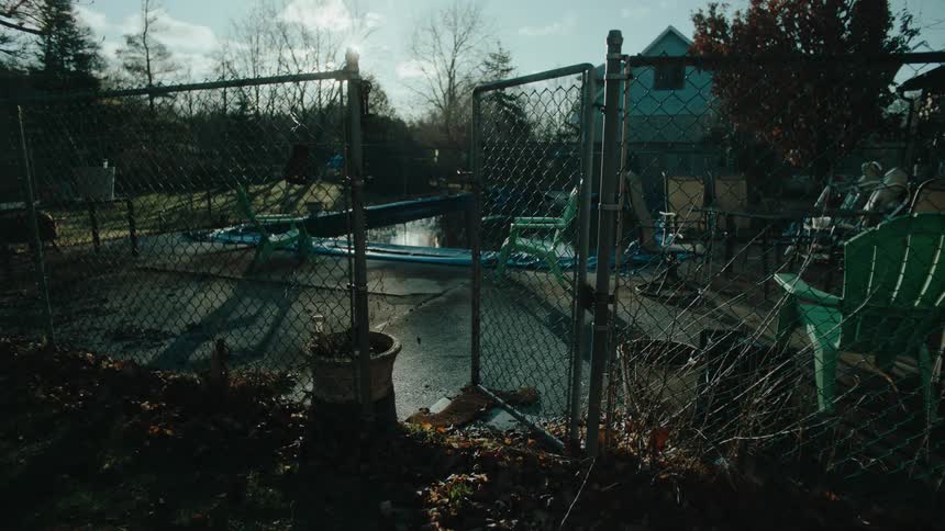 Fallen leaves pile up near the chain link fence enclosing a house with a pool