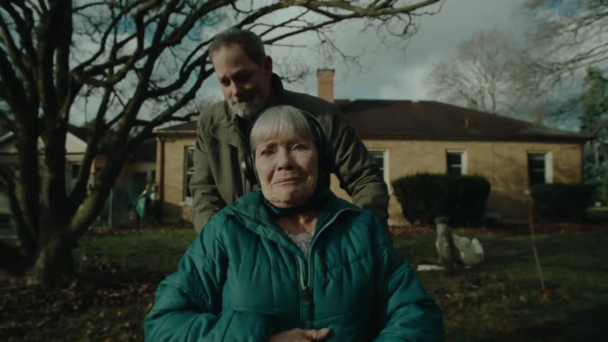 A man pushes a wheelchair with an elderly woman in the neighborhood