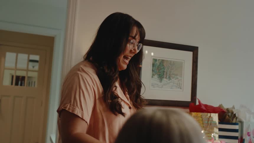 A woman brings birthday cake into the dining room and places it on the table