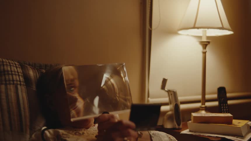 A woman looks at a photo in bed using a magnifying glass