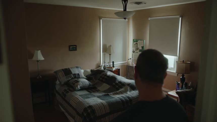 Man looks at elderly woman lying in bed in bedroom