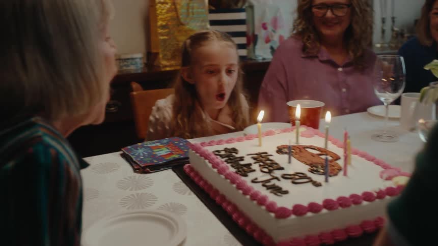 Elderly lady blowing out candles on a birthday cake together with a child by her side