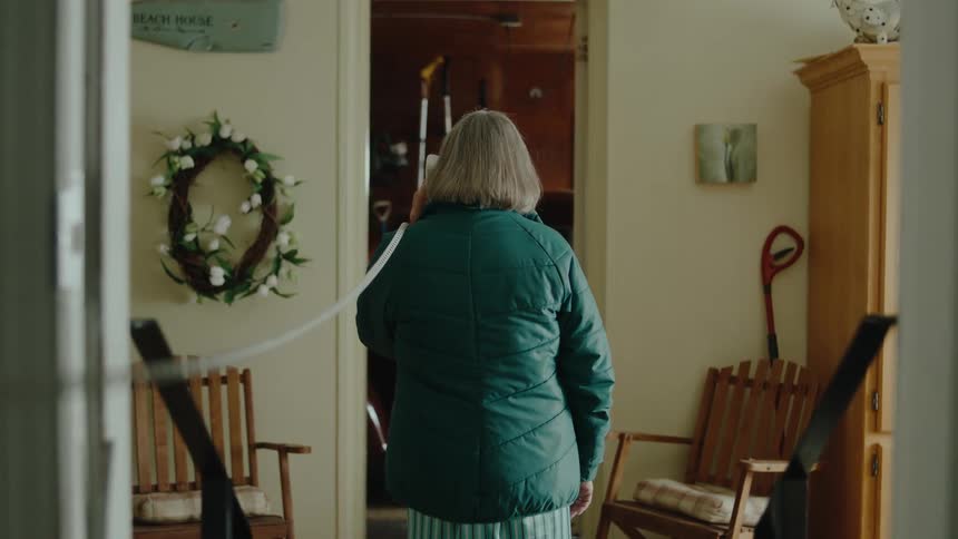 An elderly woman talking on the phone in the living room at home
