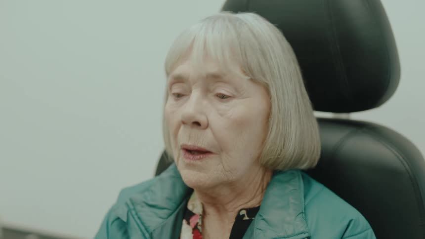 Elderly woman grooms herself while sitting in a chair