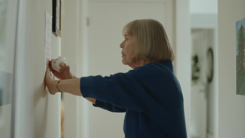 A lady placing a sticker on a white wall and guiding her eye to the paper