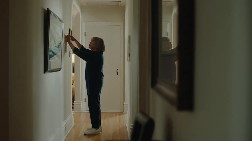 A woman is taping a piece of paper on the wall of a hallway at home