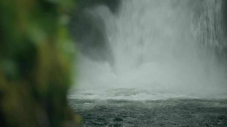 A waterfall flowing and splashing into the basin creating foam and mist