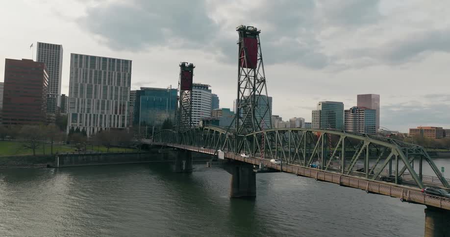 Aerial view of a cityscape with a bridge over a river and tall buildings under a cloudy sky